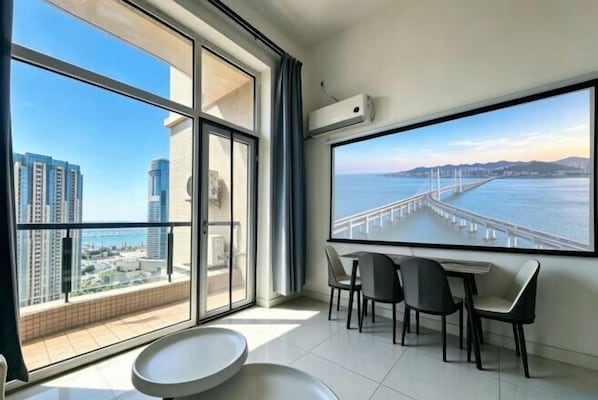 A modern room with a large window, a dining table with chairs, and an air conditioning unit.