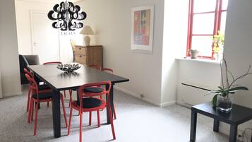 A dining area with a black table and red chairs, a chandelier, a wooden cabinet, a framed picture, and a window with plants.