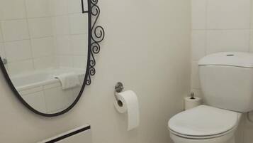 Un baño con inodoro, bidé, cubo de basura y toallero.