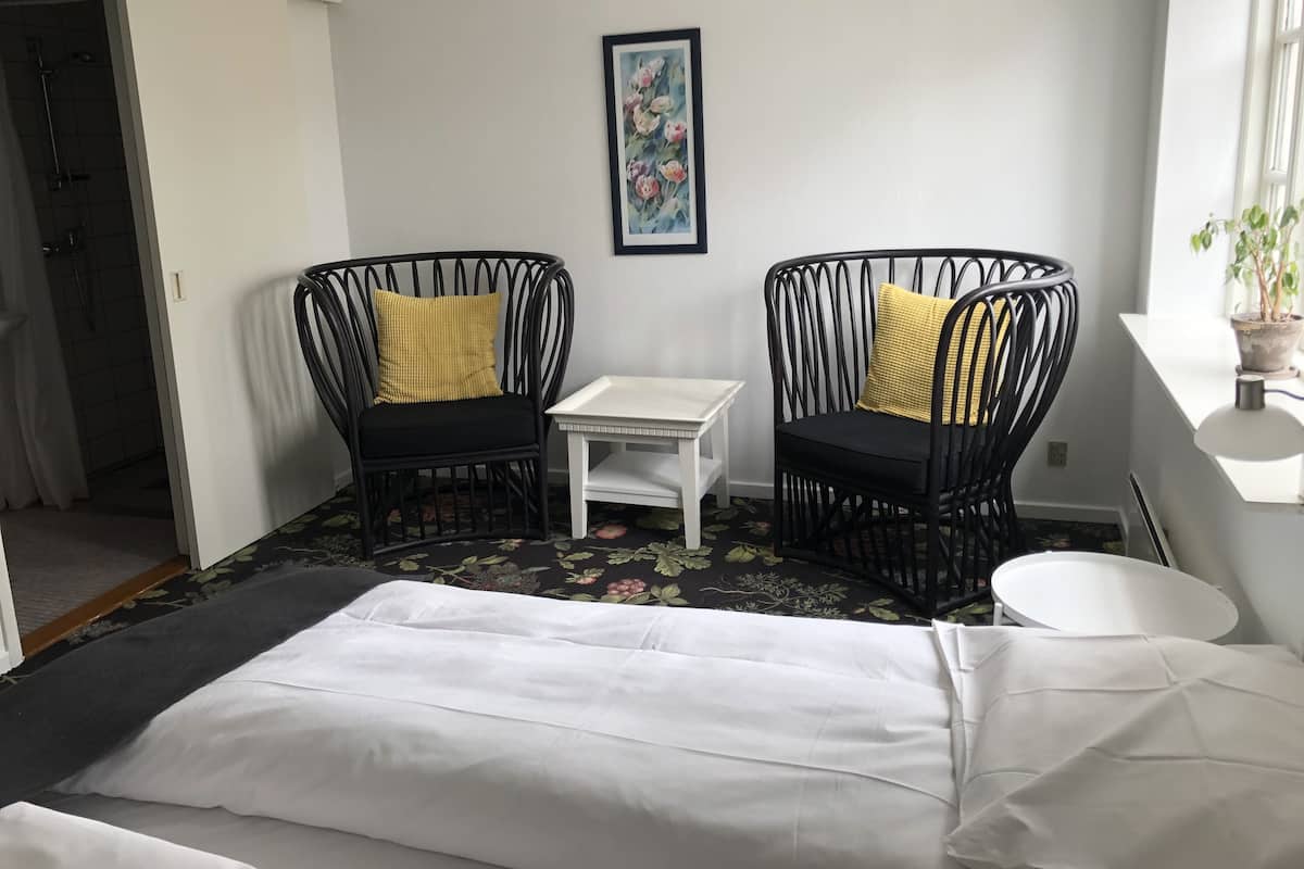 A room with two black wicker chairs with yellow cushions, a small white table, and a bed with white bedding.
