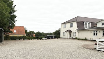 Une allée de gravier mène à une maison à deux étages, dotée d’un toit en tuiles et d’un petit porche.
