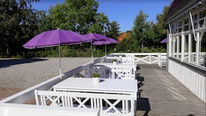 Outdoor seating with white tables and purple umbrellas, a wooden deck, and a building with large windows. - Ølsted Kro (Olsted)
