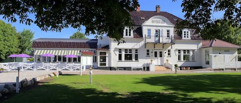 A large white building with a balcony and a sign that reads "Alsted Kro".