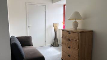 A room with a sofa, a wooden dresser, a lamp, and a tall floor lamp.
