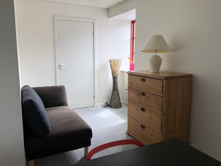 A room with a sofa, a wooden dresser, a lamp, and a tall floor lamp.