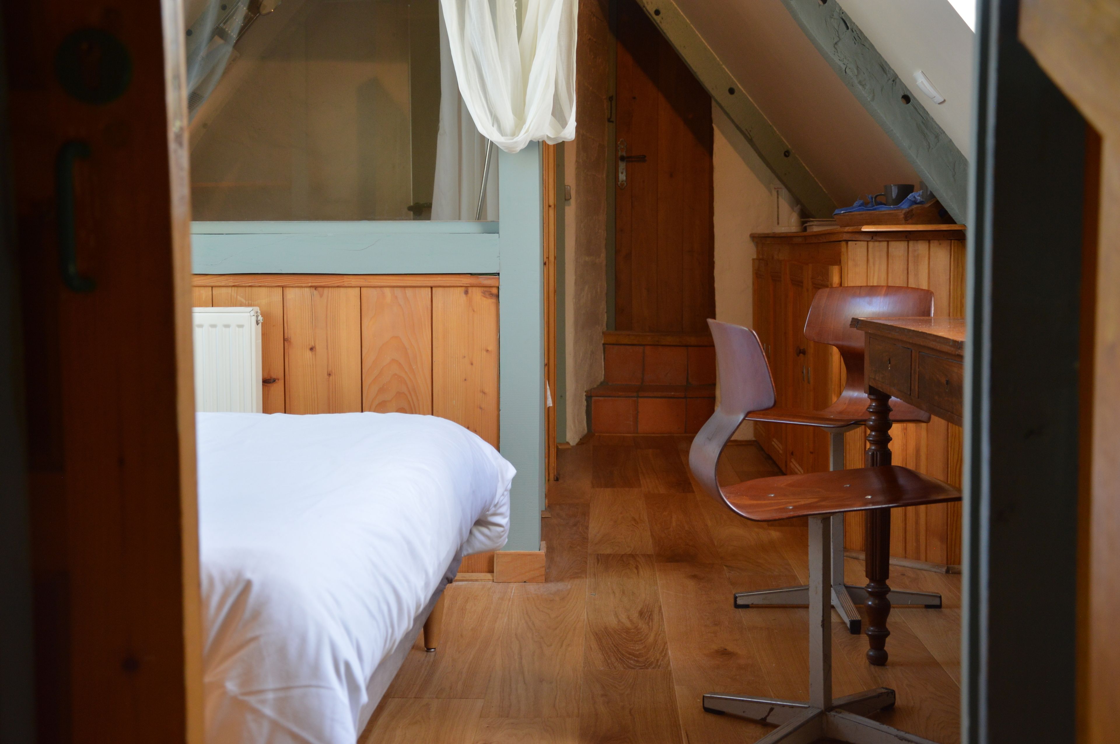 A bedroom with a bed, wooden floor, and a desk with a chair.