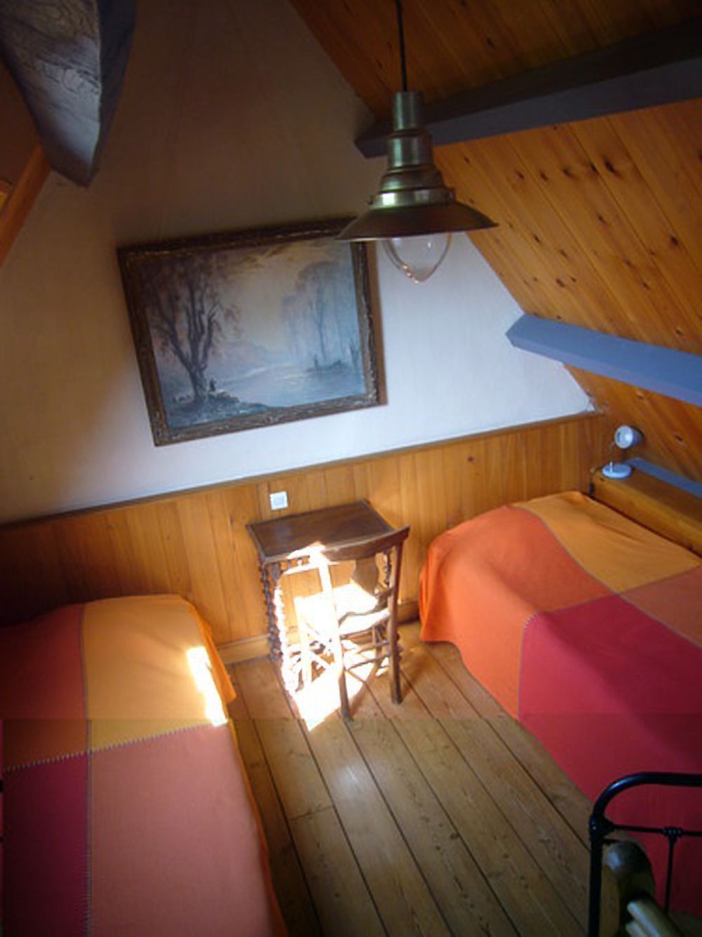 A room with two beds, a wooden ceiling, a painting, and a table with a lamp.