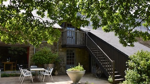 A stone building with a balcony, outdoor seating, and a large planter. - La Grange de Coatelan (Plougonven)