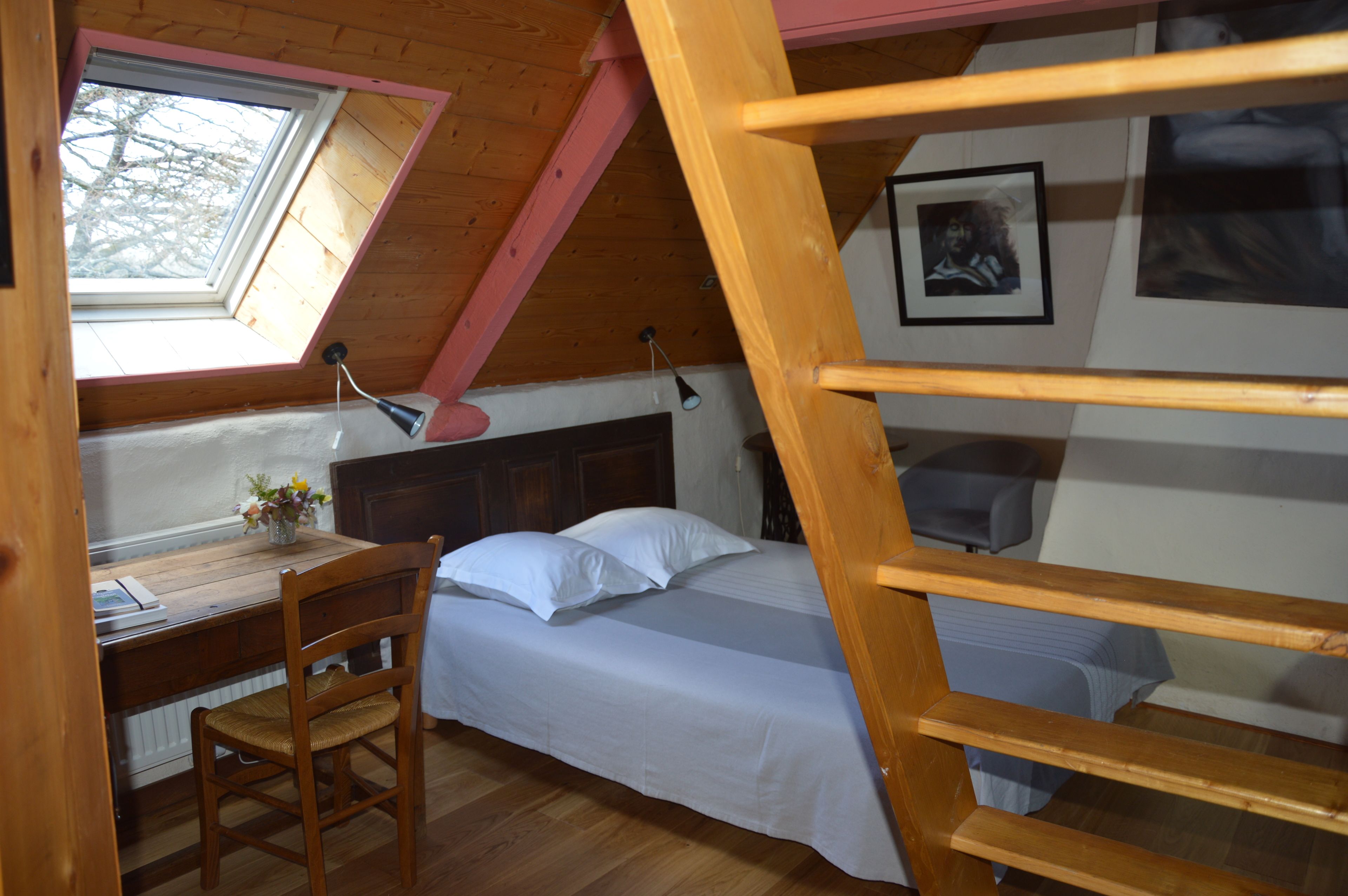 A bedroom with a loft bed, a desk with a chair, a window, and a wooden ladder.