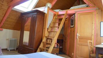 A bedroom with a sloped ceiling, a wooden wardrobe, a ladder, a radiator, and a desk with a chair.