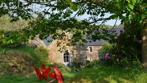 A stone building with a window and a door, surrounded by greenery and a red sculpture. - La Grange de Coatelan (Plougonven)