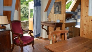 A rustic wooden interior with a dining table, a red upholstered chair, and a wooden cabinet. - La Grange de Coatelan (Plougonven)