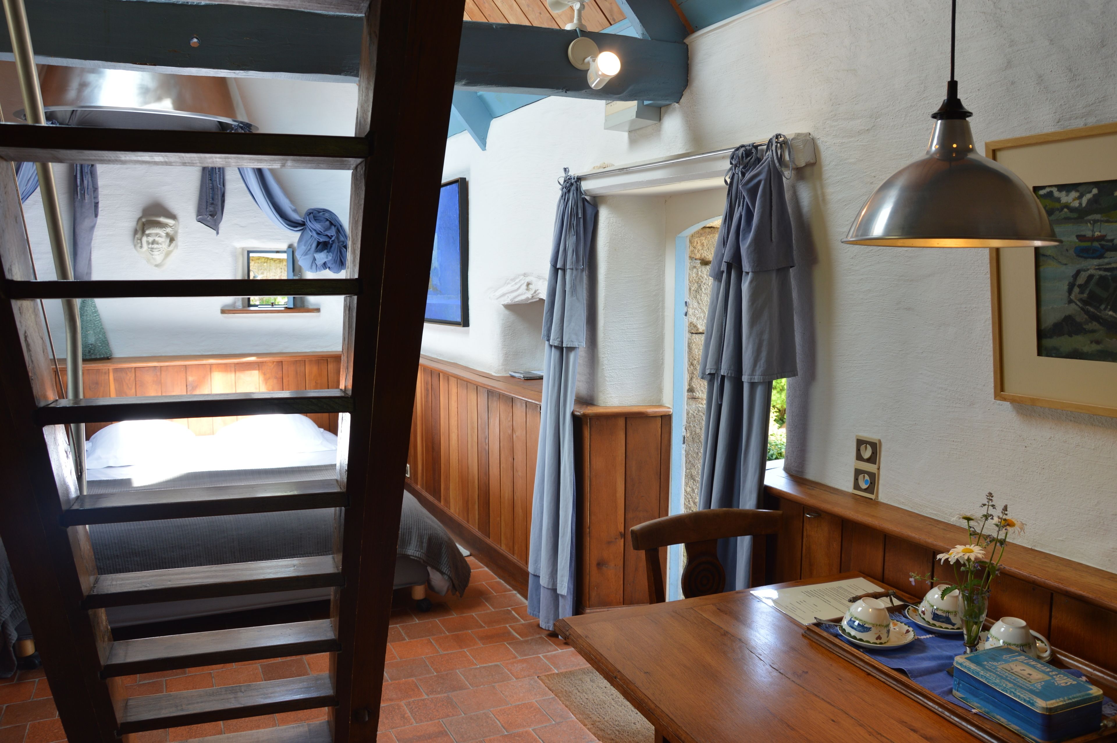 A cozy room with a wooden table, a bench, and a view of a bedroom through a wooden door.
