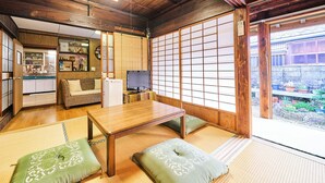 A traditional Japanese room with tatami flooring, a low wooden table, cushions, and sliding shoji doors. - Kokoyui Guesthouse (Nachikatsuura)