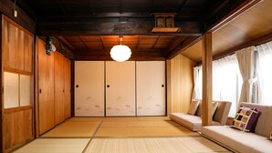 A traditional Japanese room with tatami flooring, sliding doors, and a sofa with cushions. - Kokoyui Guesthouse (Nachikatsuura)