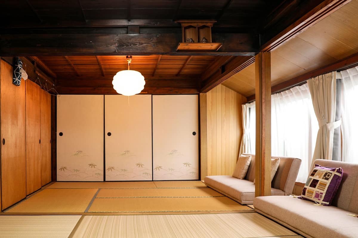 Ein traditioneller japanischer Raum mit Tatami-Bodenbelag, Schiebetüren und einer Couch mit Kissen.