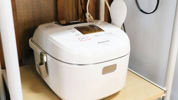 A white Panasonic rice cooker with a digital display, placed on a wooden shelf.