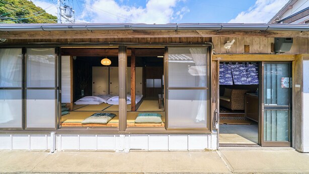 A traditional Japanese-style room with tatami mats, a futon bed, sliding doors, and a view of a mountain. - Kokoyui Guesthouse (Nachikatsuura)