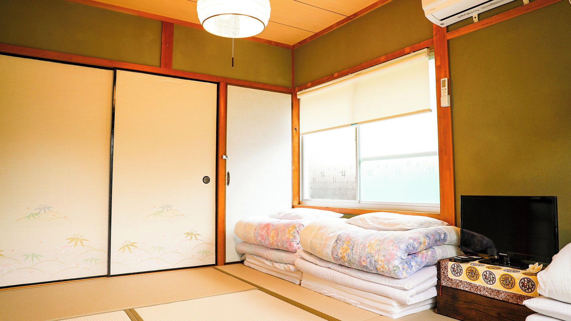 A traditional Japanese room with tatami flooring, a futon bed, sliding doors, and a large window.