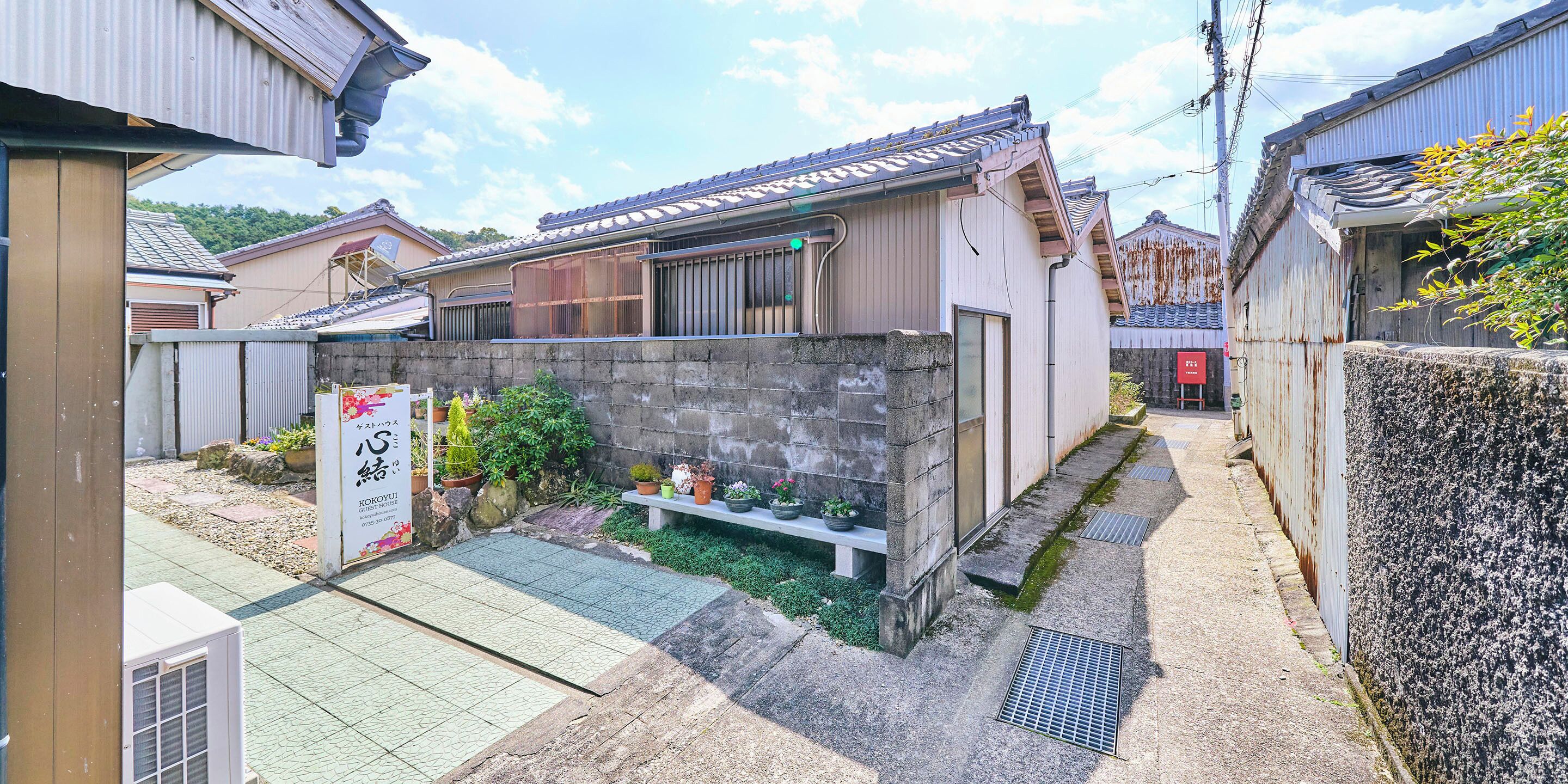 A traditional Japanese house with a tiled roof, a stone wall, and a small garden area with potted plants.