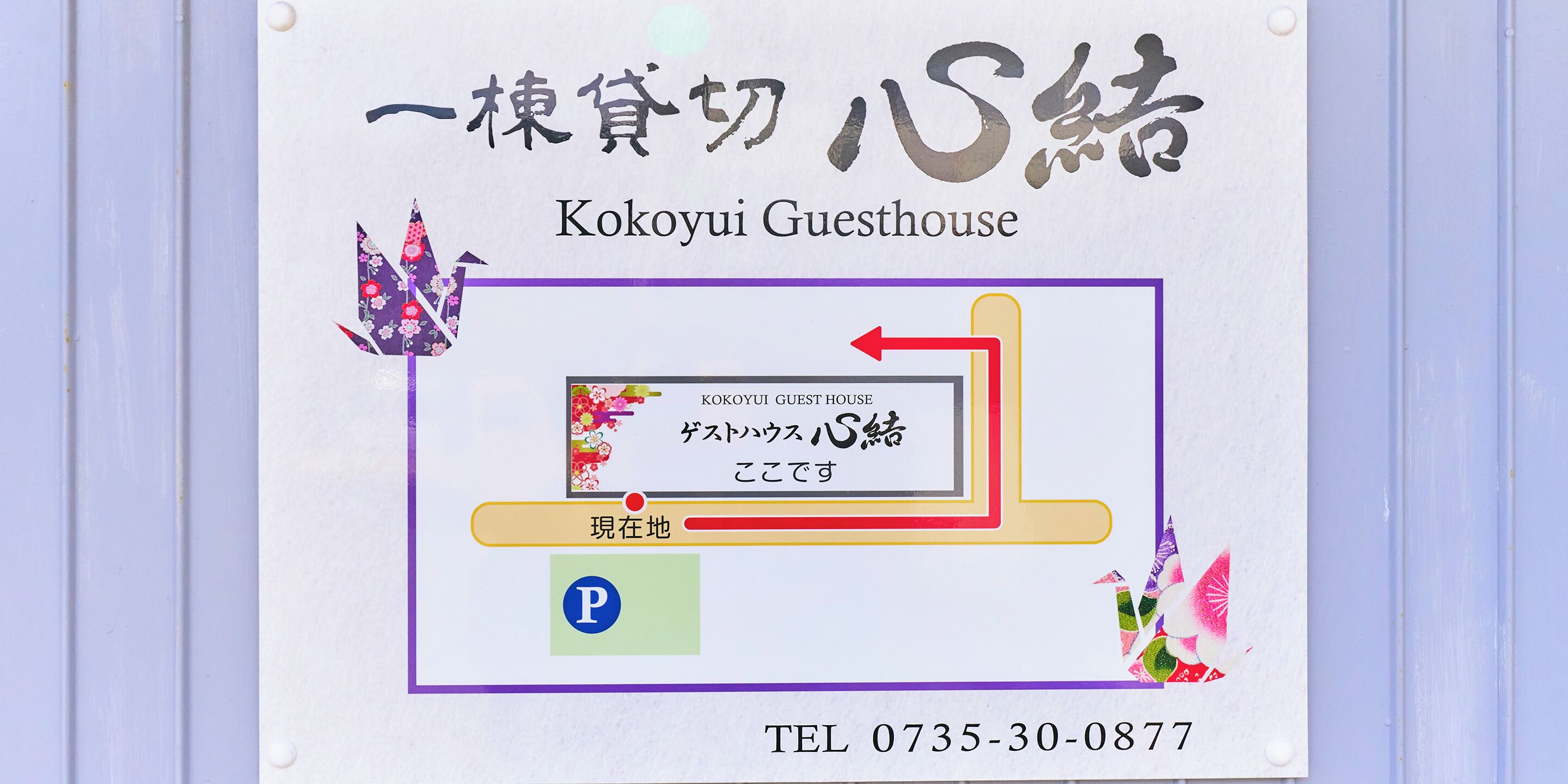 A sign for Kokoyui Guesthouse with Japanese text, a directional arrow, and a parking symbol.