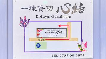 A sign for Kokoyui Guesthouse with Japanese text, a directional arrow, and a parking symbol.