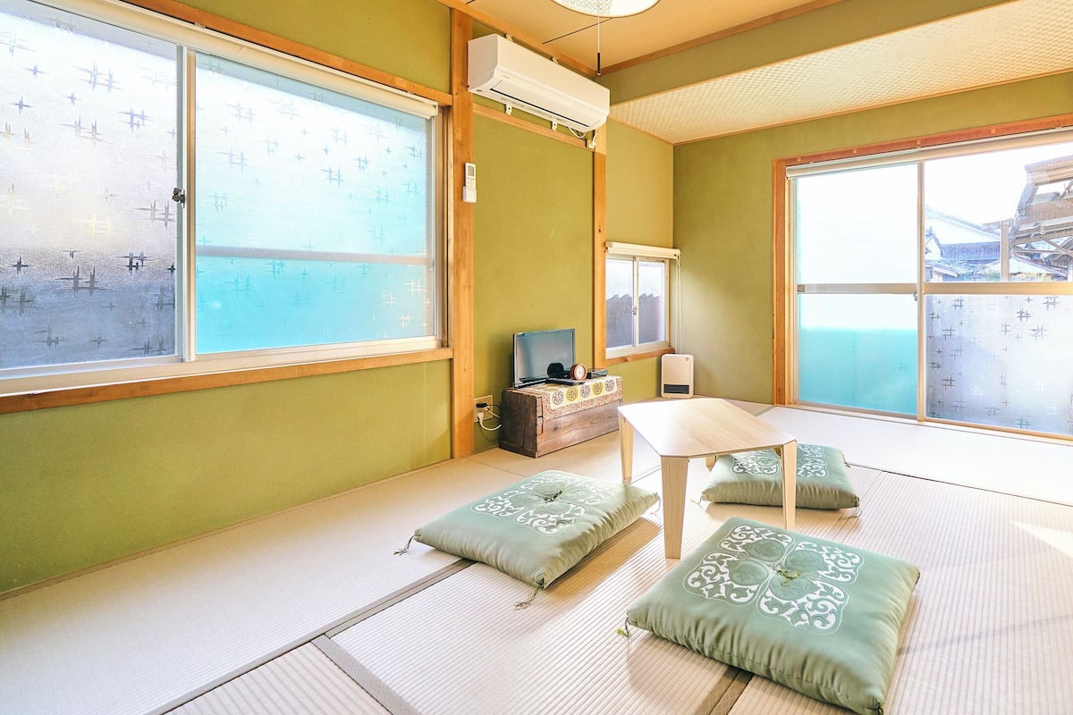 Ein Raum mit Tatami-Matten, einem Holztisch, Kissen und einem Fernseher.