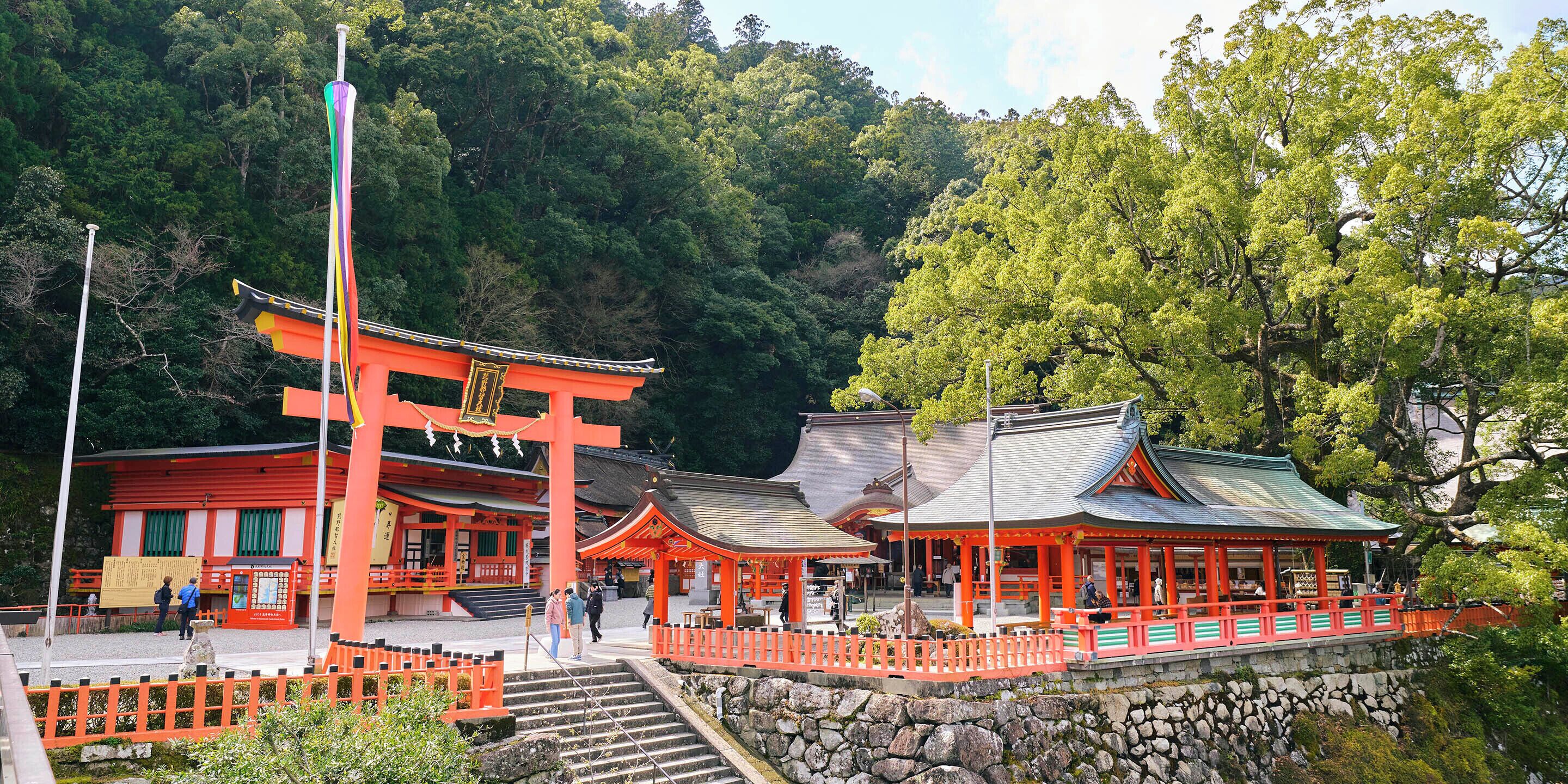 Un templo japonés tradicional con una destacada puerta torii, escalones de piedra y un muro de piedra que rodea el área.