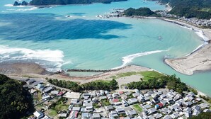 An aerial view of a coastal residential area with houses, a beach, and a rocky shoreline. - Kokoyui Guesthouse (Nachikatsuura)