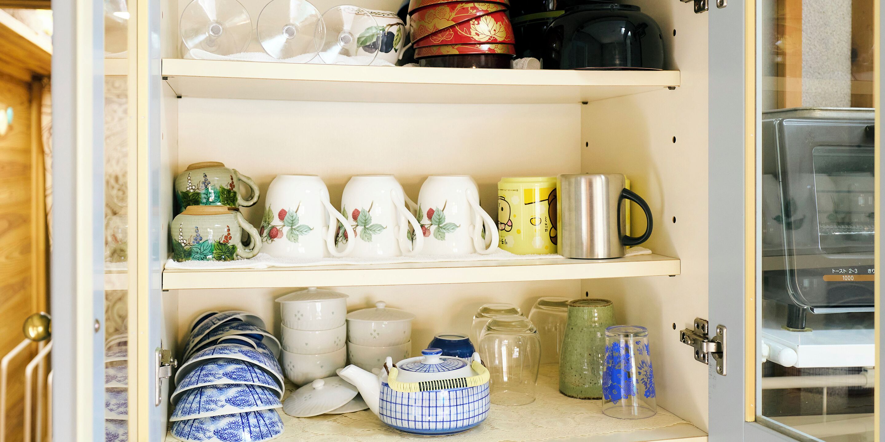 A kitchen cabinet with various kitchenware including teapots, cups, and jars.