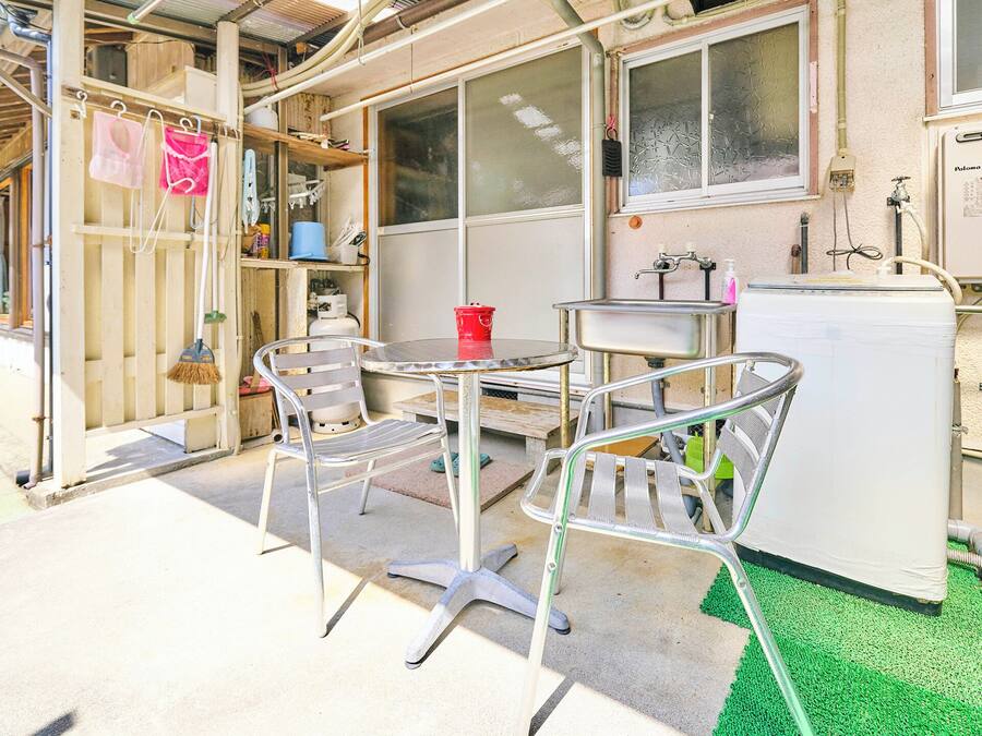 A small outdoor area with a metal table and chairs, a red bucket, a white refrigerator, and a large potted plant.
