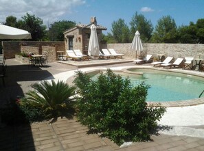 A pool area with lounge chairs and umbrellas, a small stone building, and surrounding greenery. - Residence Borgo da Mare (Monteprandone)