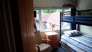 Una habitación pequeña y compacta con una litera, una silla, un pequeño aparador de madera y una ventana que ofrece vistas al exterior.