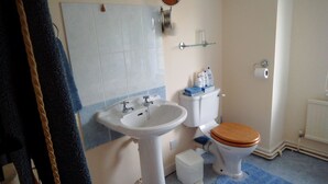 Un baño con un lavabo blanco, un inodoro de madera y un tapete azul en el suelo.