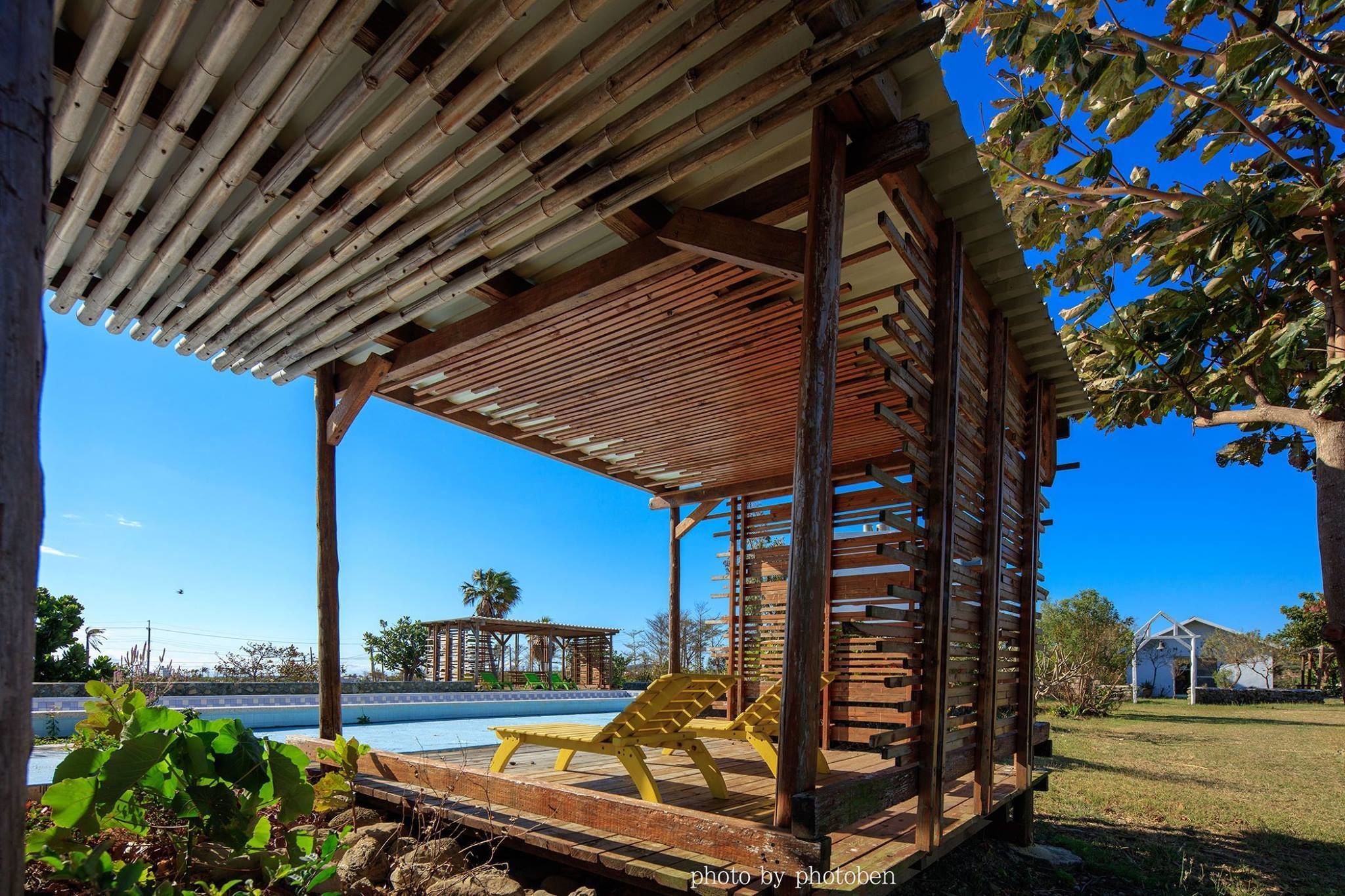 A covered outdoor seating area with a pool in the background.