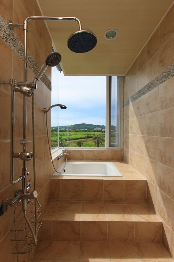 A modern bathroom with a glass-enclosed shower, a bathtub, and a view of a green landscape. - Wild Island B&B (Hengchun)