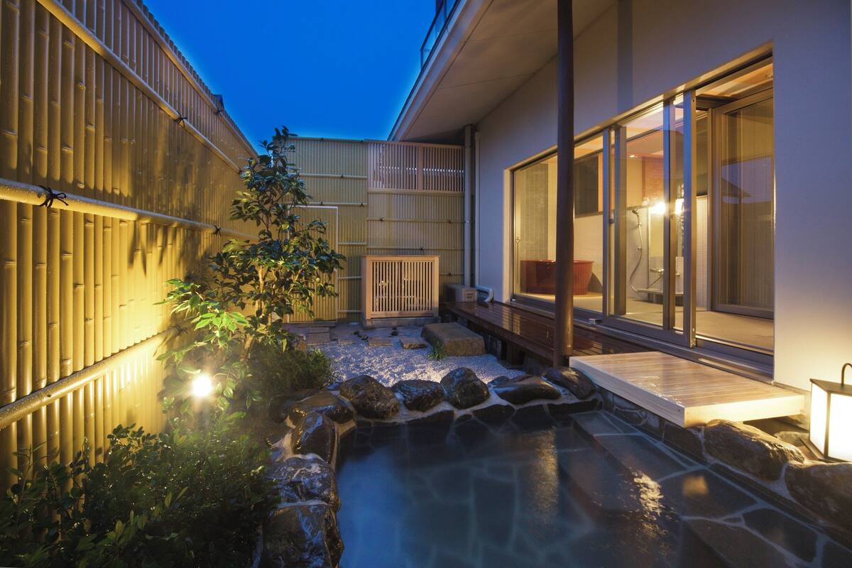Um pátio japonês tradicional com um recurso de água em pedra, cercas de bambu e um deck de madeira.