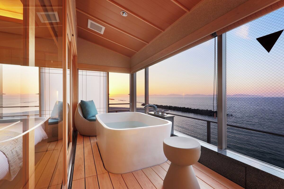 Quarto moderno com uma banheira grande, área de estar e vista para o mar.