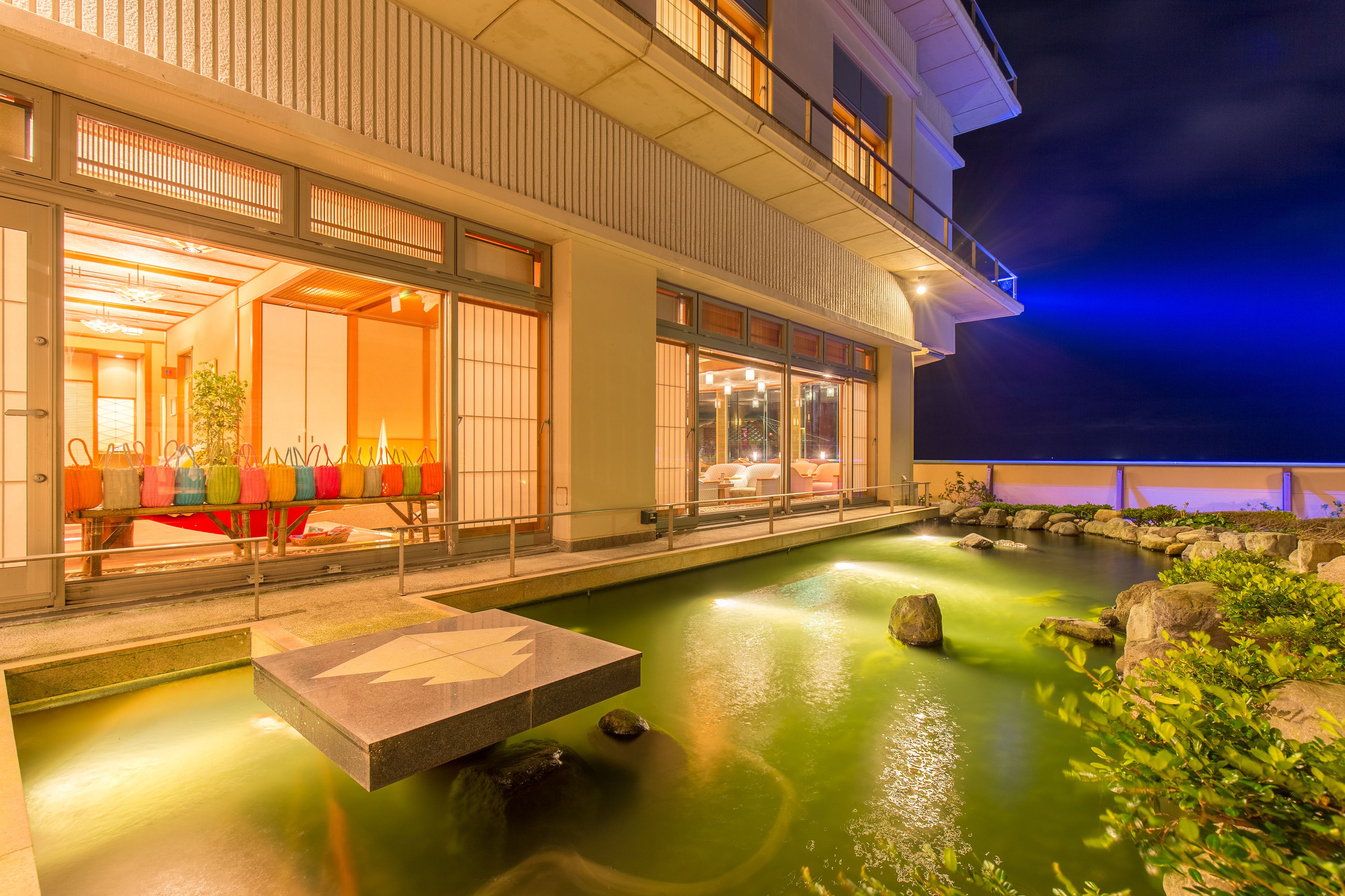A hotel with a koi pond, indoor seating area, and a view of the night sky.