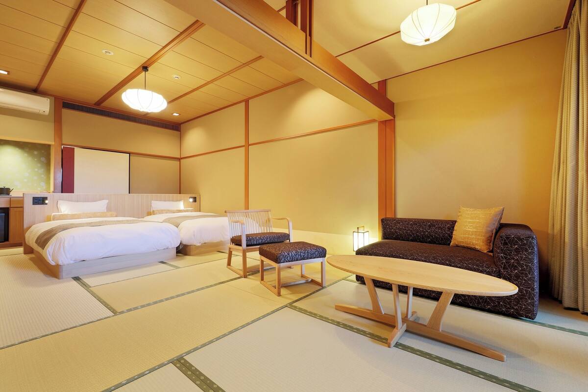 Quarto de hotel em estilo japonês tradicional, com tatames, futon, mesa baixa e sofá.