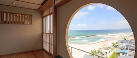 A room with a large circular window overlooking a beach and ocean.