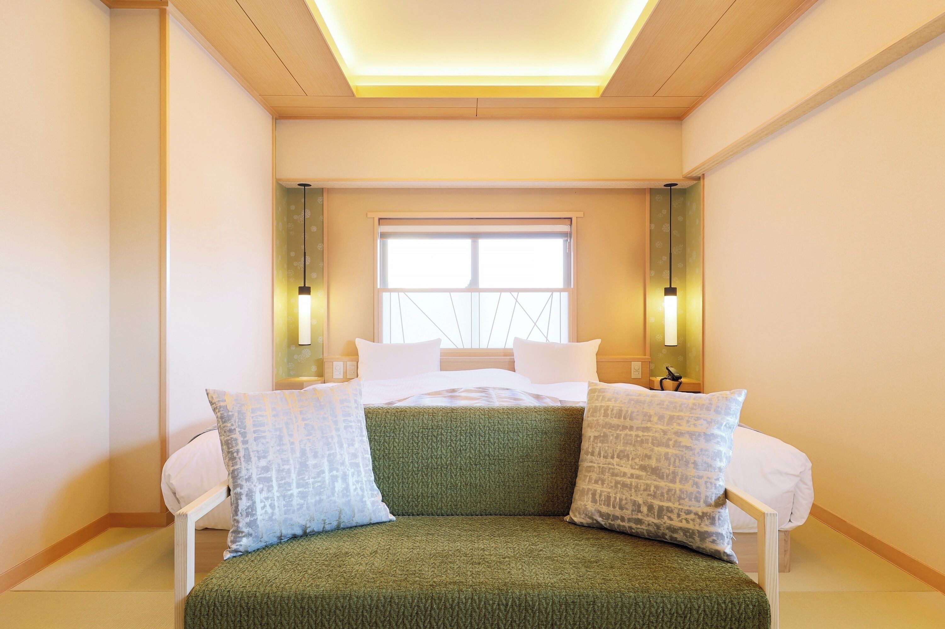 A hotel room with a bed, a green sofa, a window, and two wall-mounted lamps.