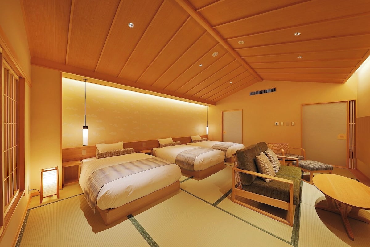 Quarto japonês tradicional com tatames, duas camas, uma mesinha e uma cadeira.