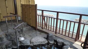 Una piscina de piedra con cubierta de madera, cerca de una valla de bambú, y vista al mar.