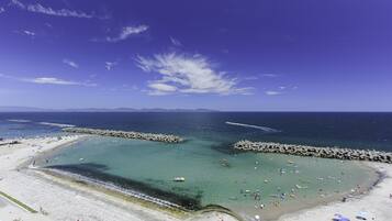 A beach with clear waters, rocky breakwaters, and a wide sandy area with umbrellas.