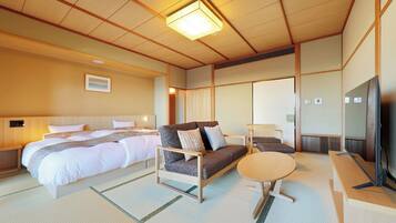 A traditional Japanese-style room with tatami flooring, a bed with white bedding, a sofa with cushions, a small round table, and a television.