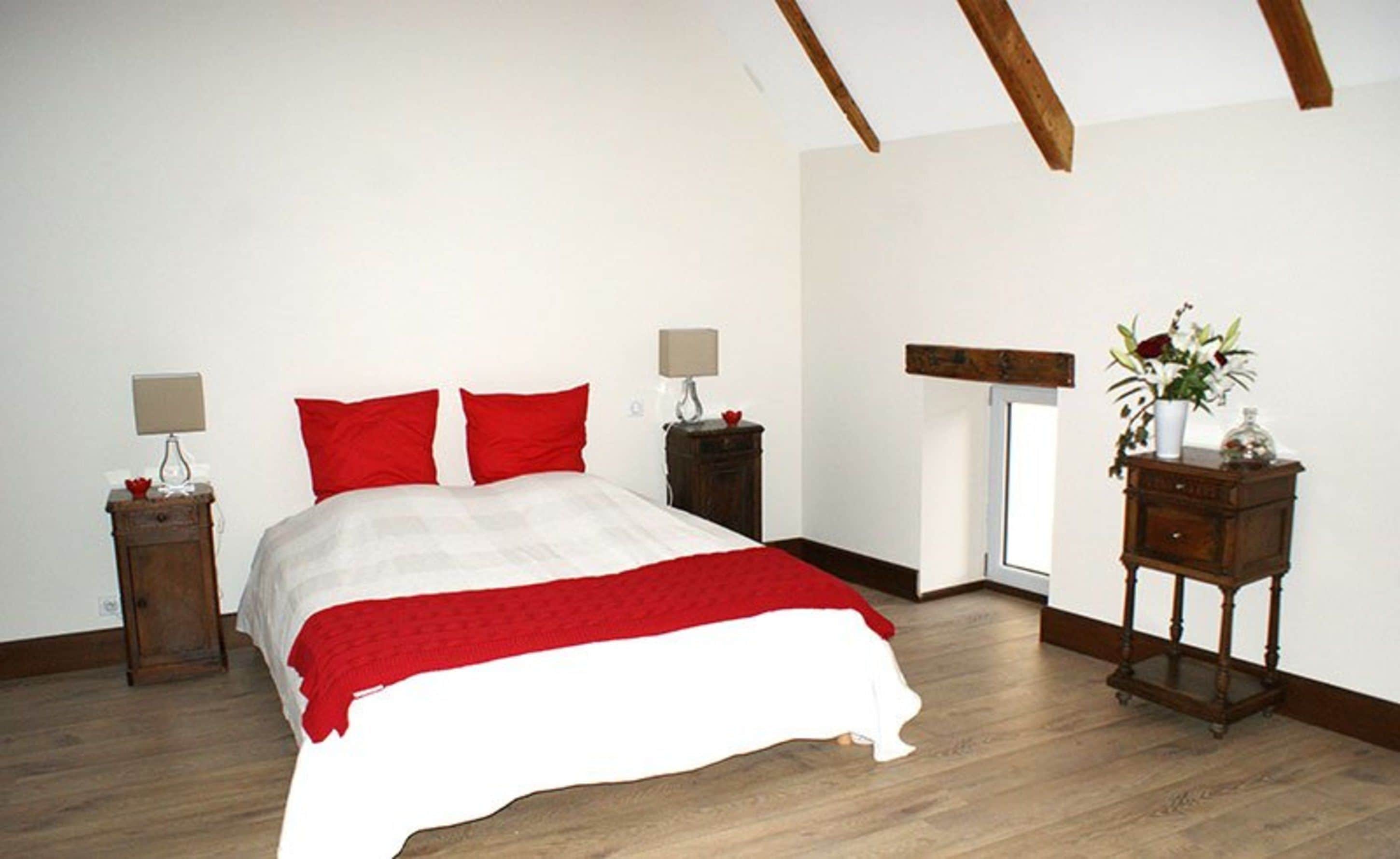 A bedroom with a bed, two bedside tables, a nightstand, a wooden bench, and a window.