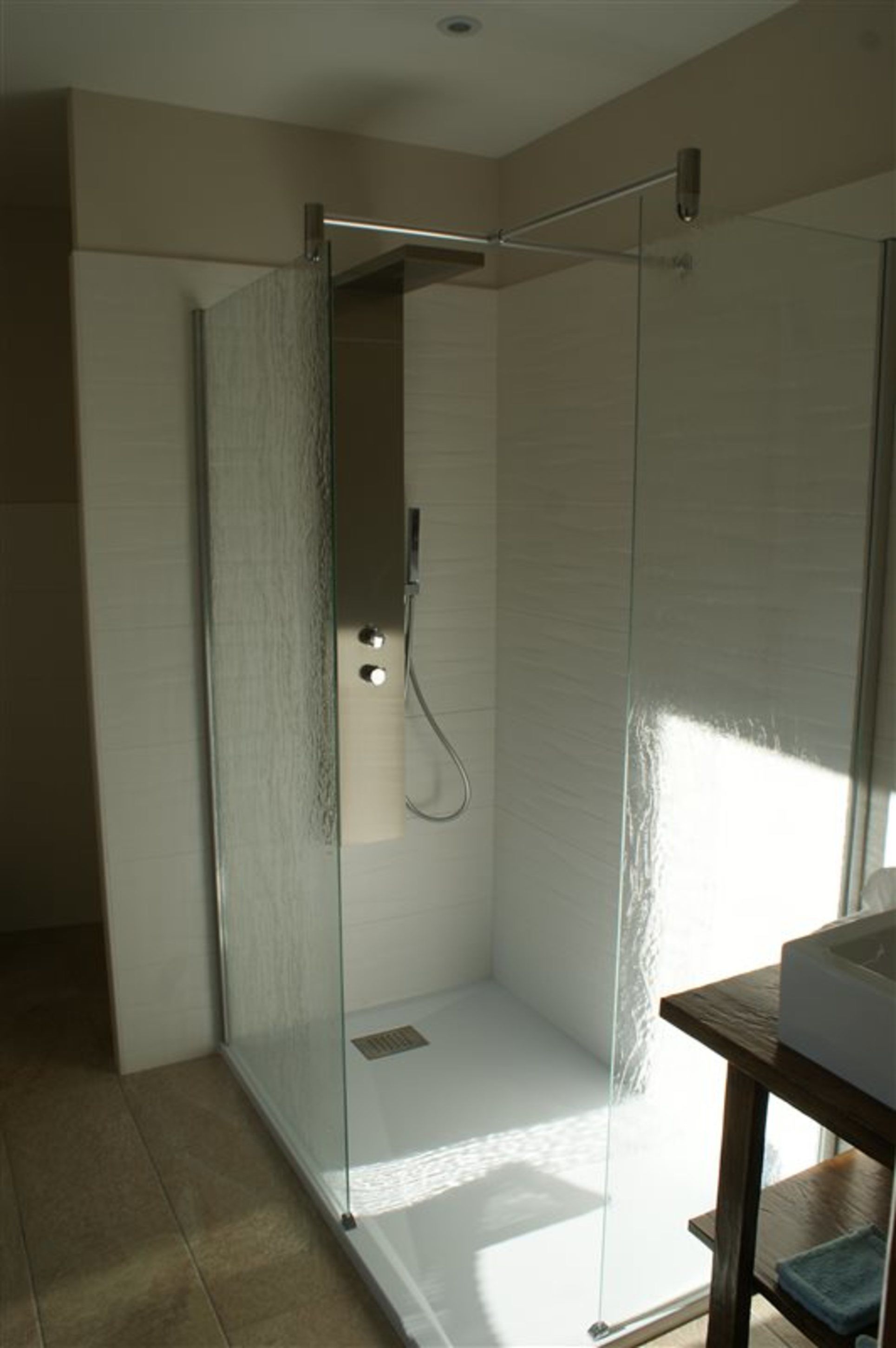 A modern bathroom with a glass-enclosed shower, a wooden vanity, and a tiled floor.