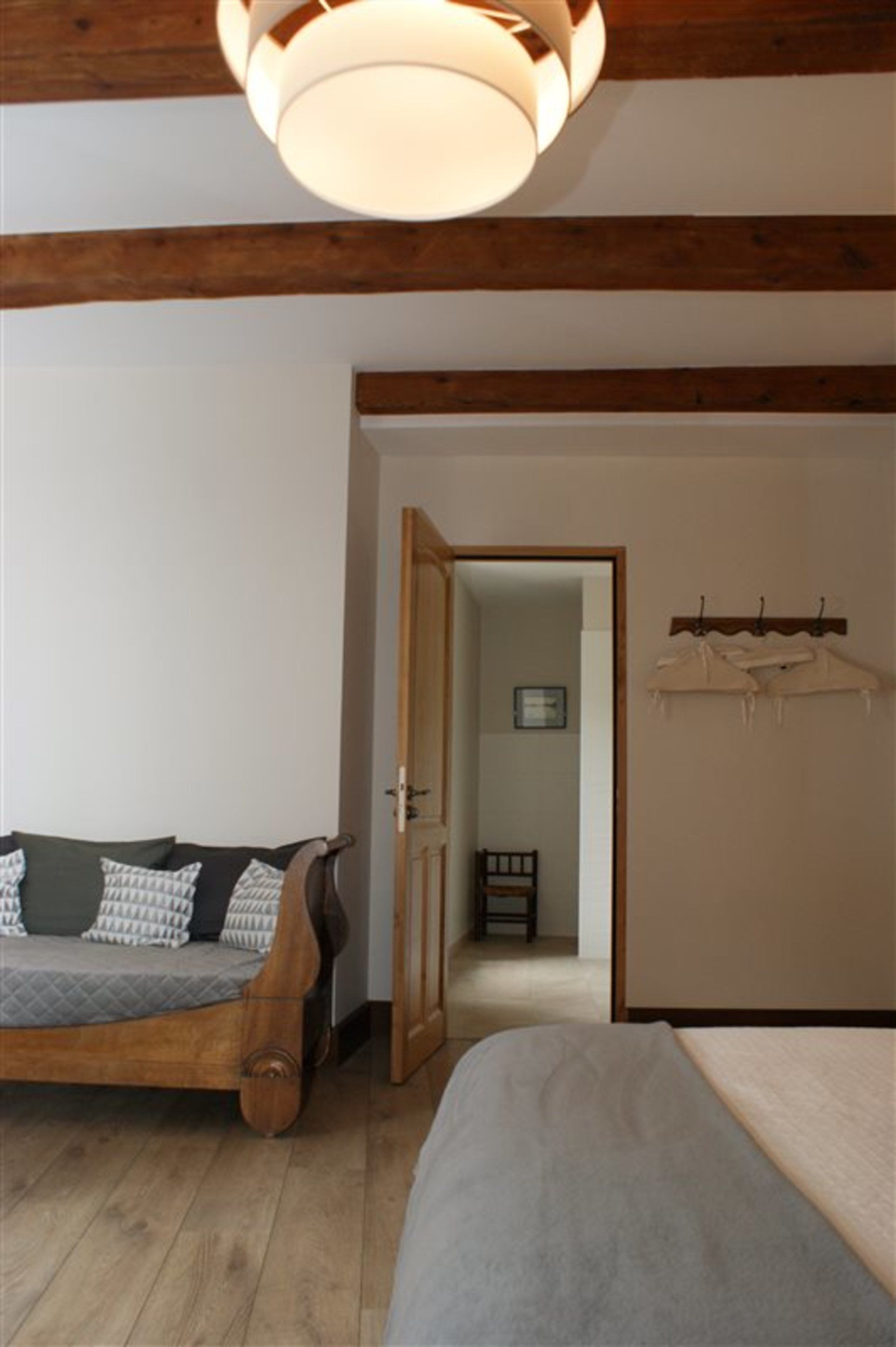 A room with a wooden bed, a sofa, a hanging light fixture, and a door leading to another room.