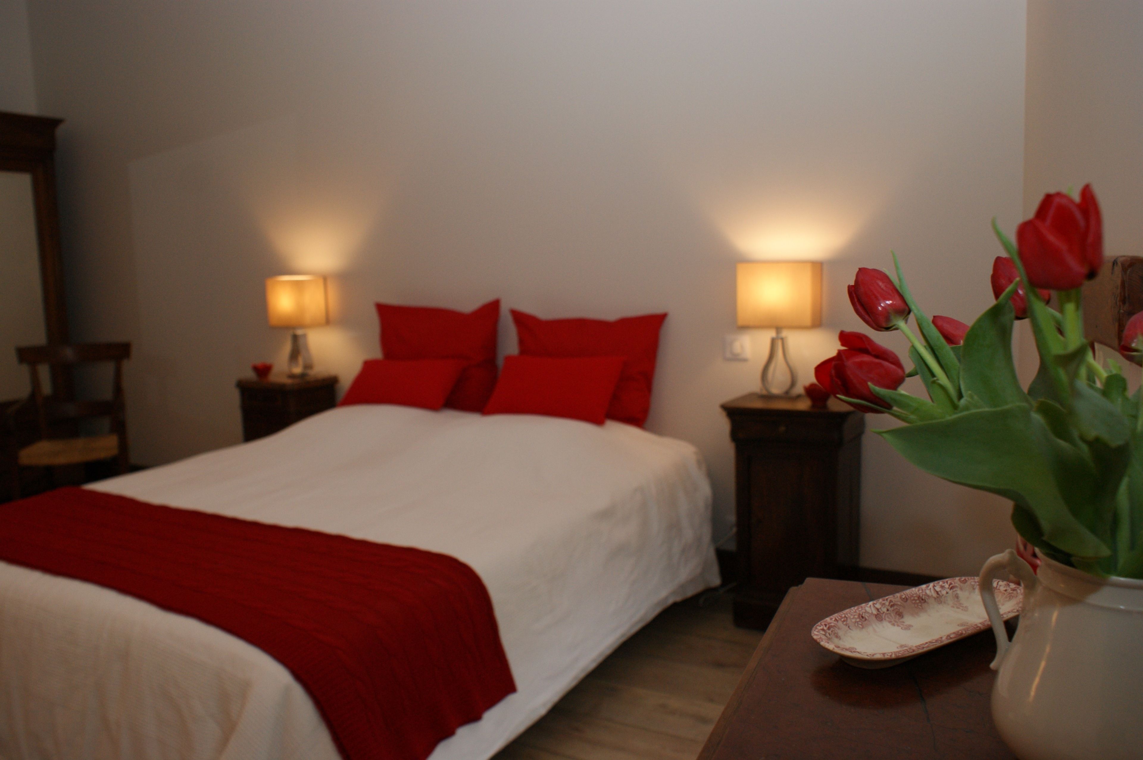 A neatly made bed with red and white bedding, two bedside lamps, and a vase with red tulips on a wooden nightstand.